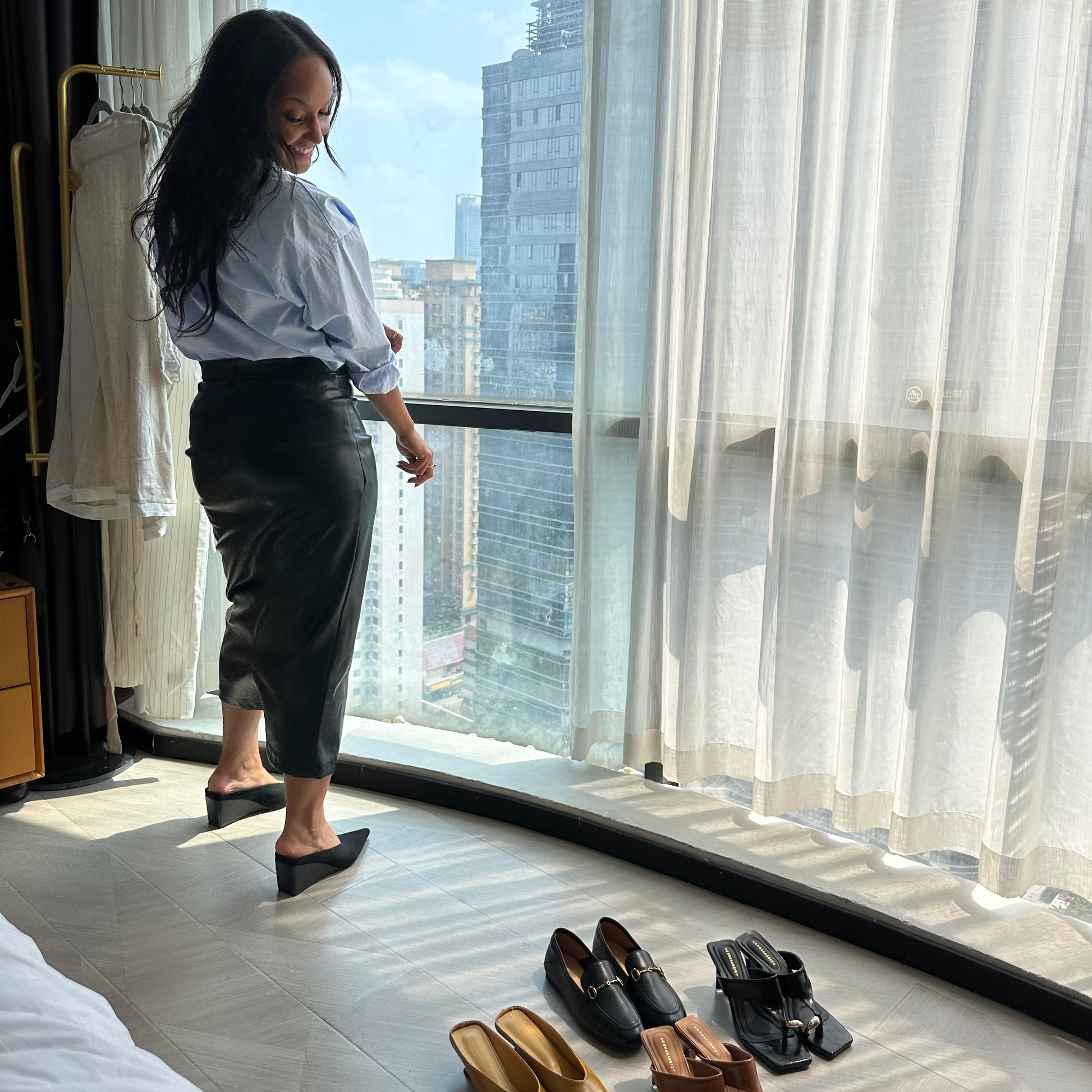 Lisa Viola standing in front of a high rise hotel window, looking at Sunset Park shoes on the floor.
