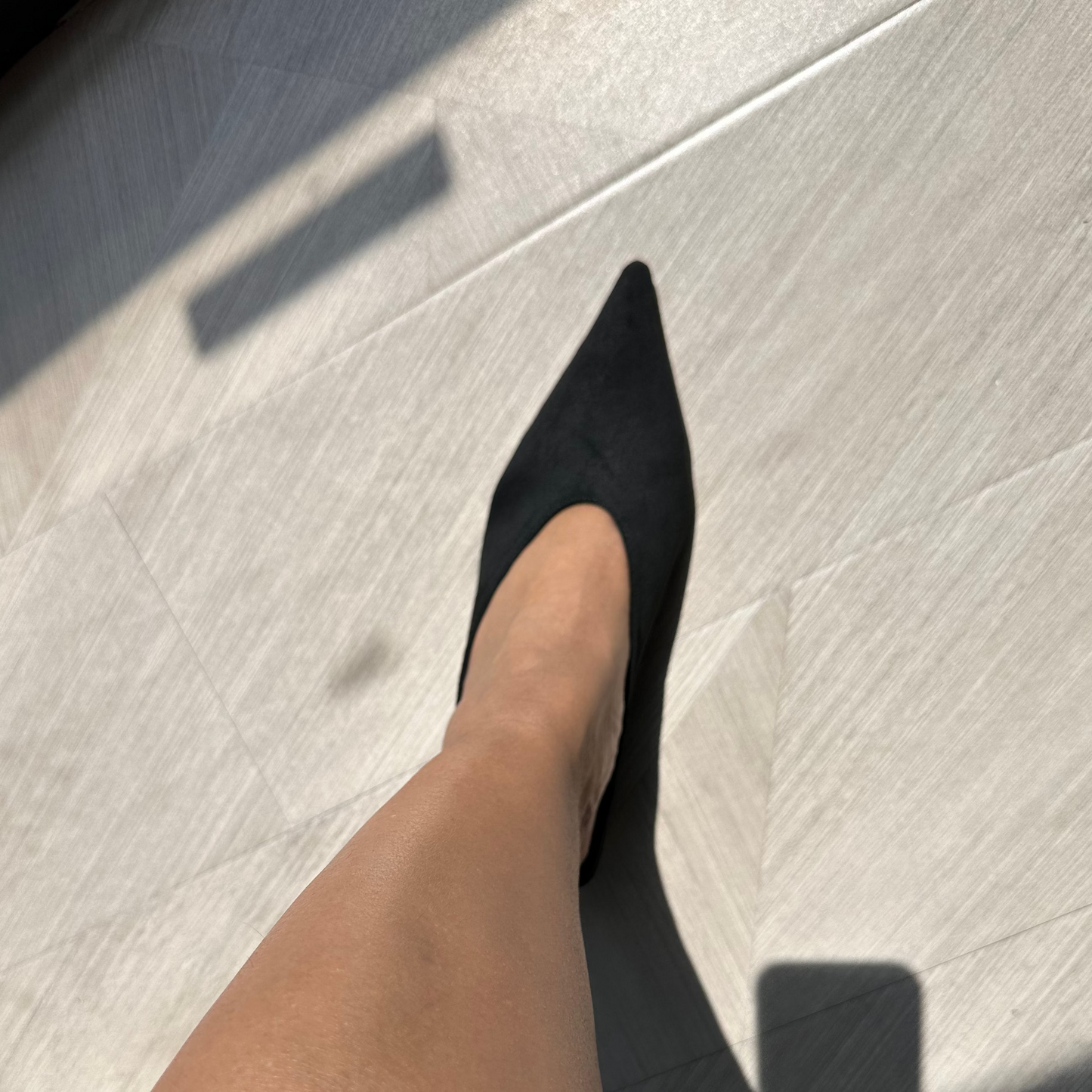 Person wearing a black pointed-toe mule shoe on a light gray tiled floor.